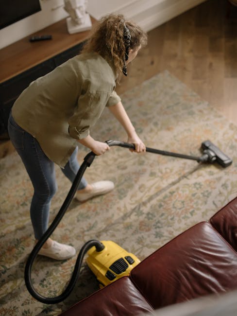 The image depicts a living room corner with polished wooden flooring partially covered by a decorative, patterned area rug. In front of a black metal and wood media console, which holds a small sculpt