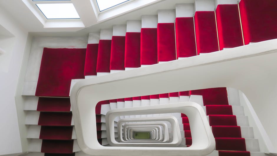 Image of a modern, multi-level residential staircase with white concrete steps and black metal railings, featuring multiple landings and staircases connecting different floors. The staircase is situat
